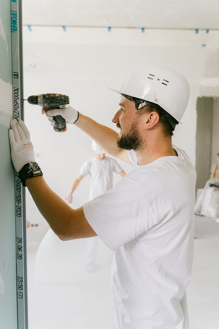 Adult male in safety gear using a power drill on a construction site indoors.